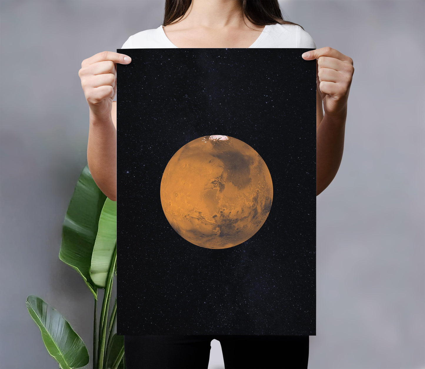 A person is holding up a framed print of a planet, specifically Mars, against a black background with stars.