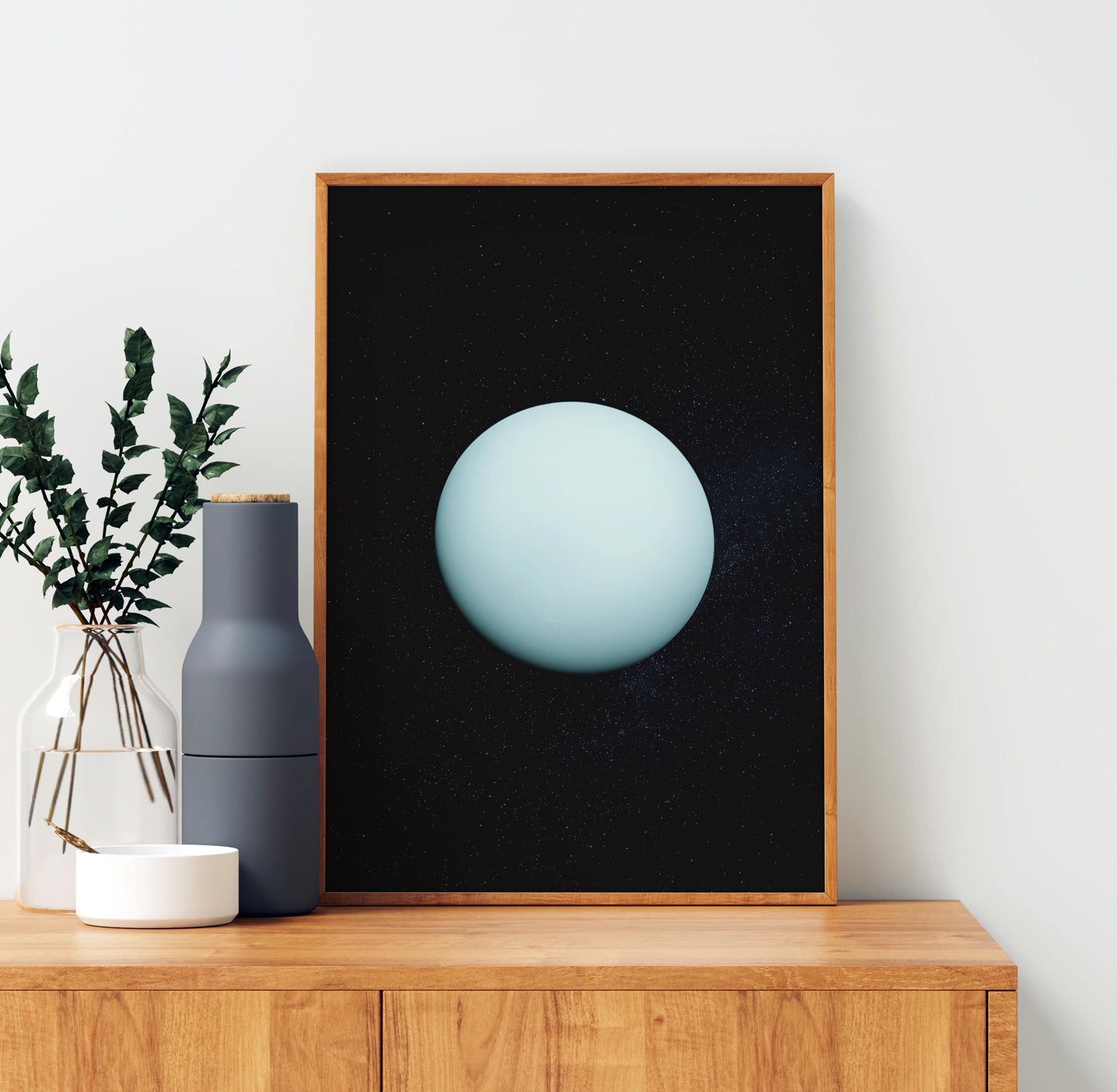 a wooden cabinet with a framed artwork of a blue planet on it, placed on a shelf next to a vase with green leaves.