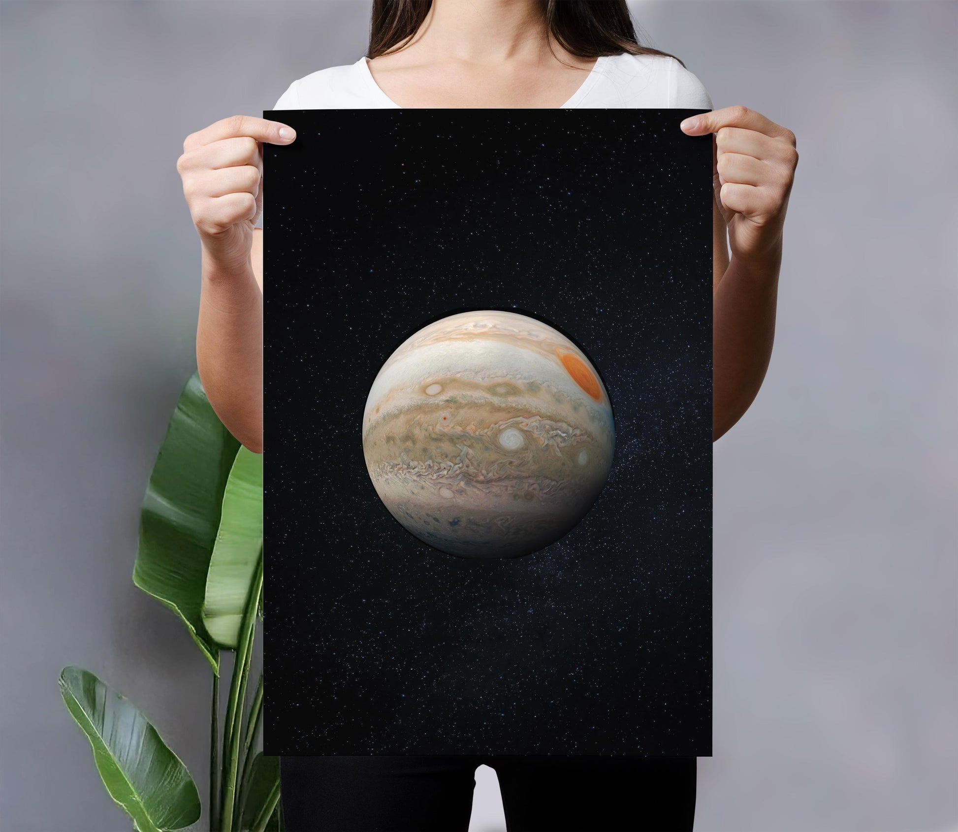 A person is holding up a framed print of a planet against a black background with stars.
