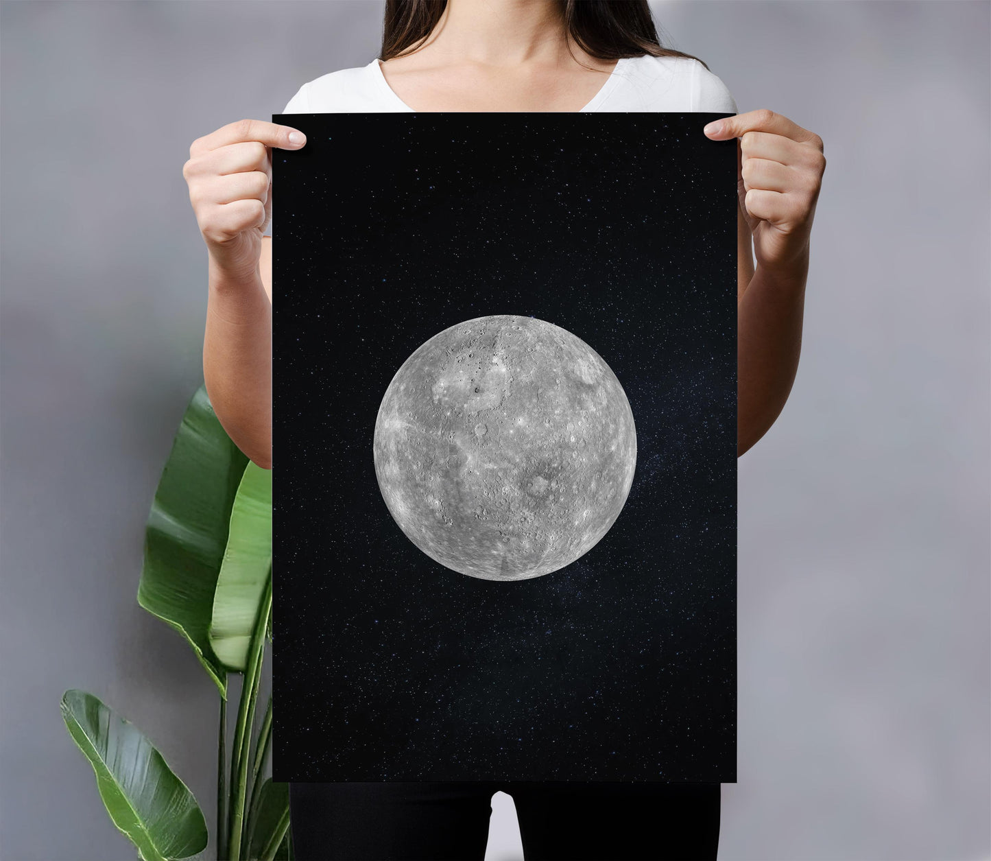 A woman holds up a framed print of a large, detailed image of the moon against a dark background.