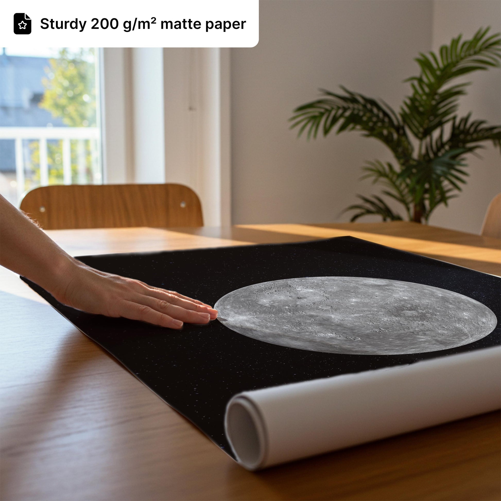 a hand resting on a black mat with a large, detailed image of the moon on it, placed on a wooden table.